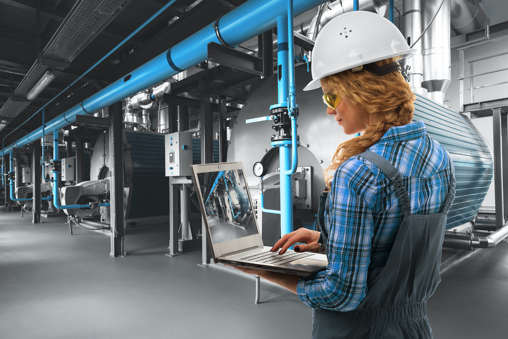 Engineer woman with laptop inspect modern industrial gas boiler room. Heating gas boilers, pipelines, valves. Mixed media