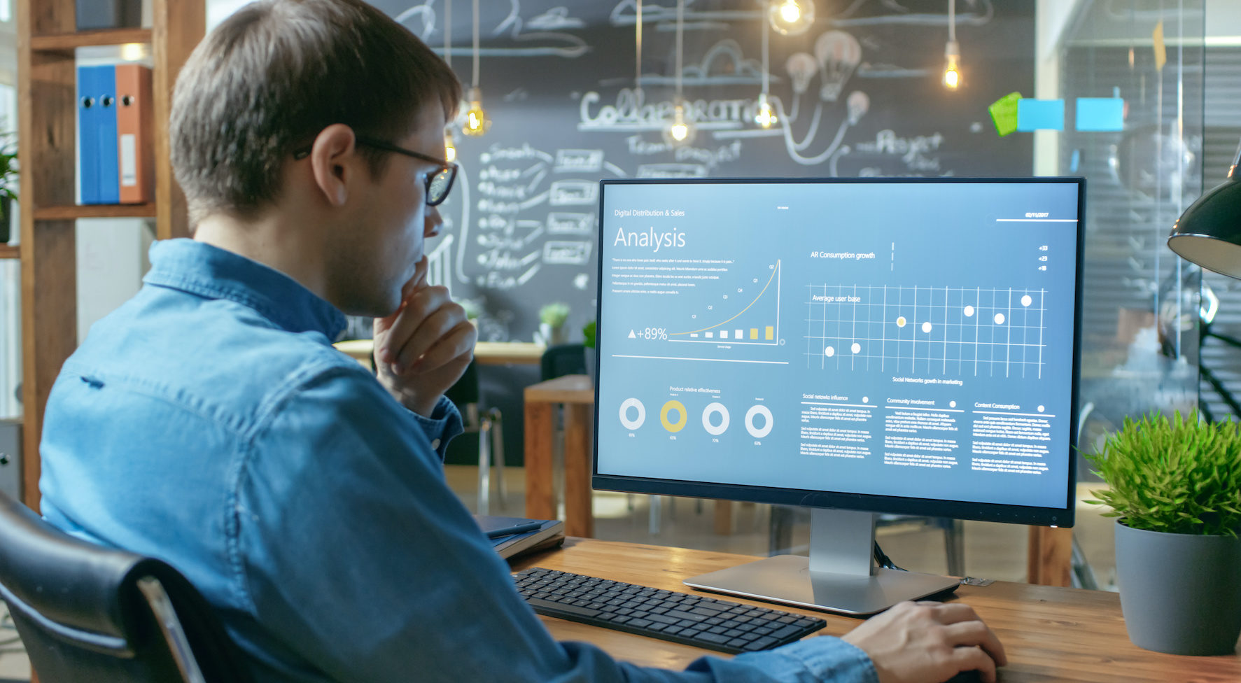 Financier Works on a Personal Computer Showing Statistics, Graphs and Charts. In the Background His Coworker and Creative Office.