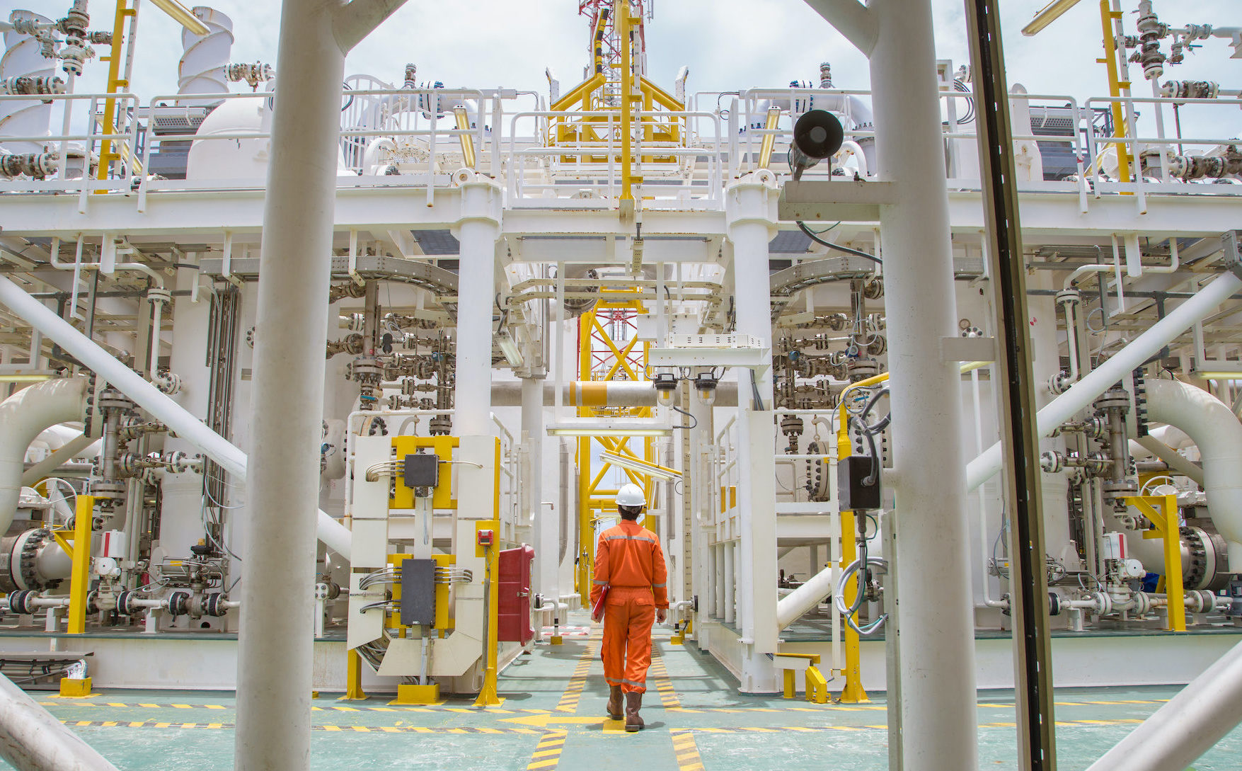 Technician walking through offshore oil and gas process for checking the condition of equipment on platform.