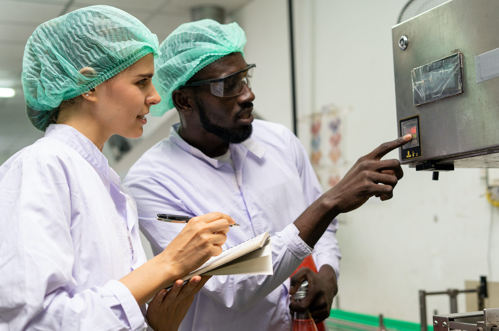 A quality supervisor or food technician explains the use of the Shrink Tunnel Machine to the new employee. Quality inspectors work together in the food factory to inspect food quality in standards.