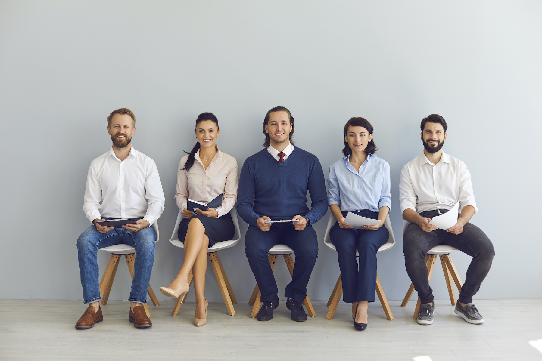 Smiling candidates job seekers sitting in row with resumes in hand and waiting for interview invitation turn