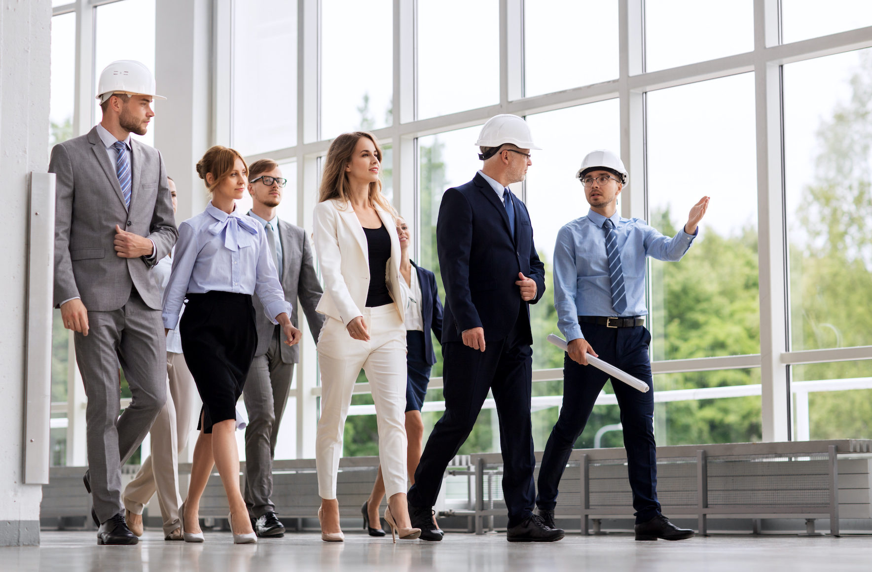 architecture, construction business and building concept - happy group of architects in helmets with blueprint walking along office building