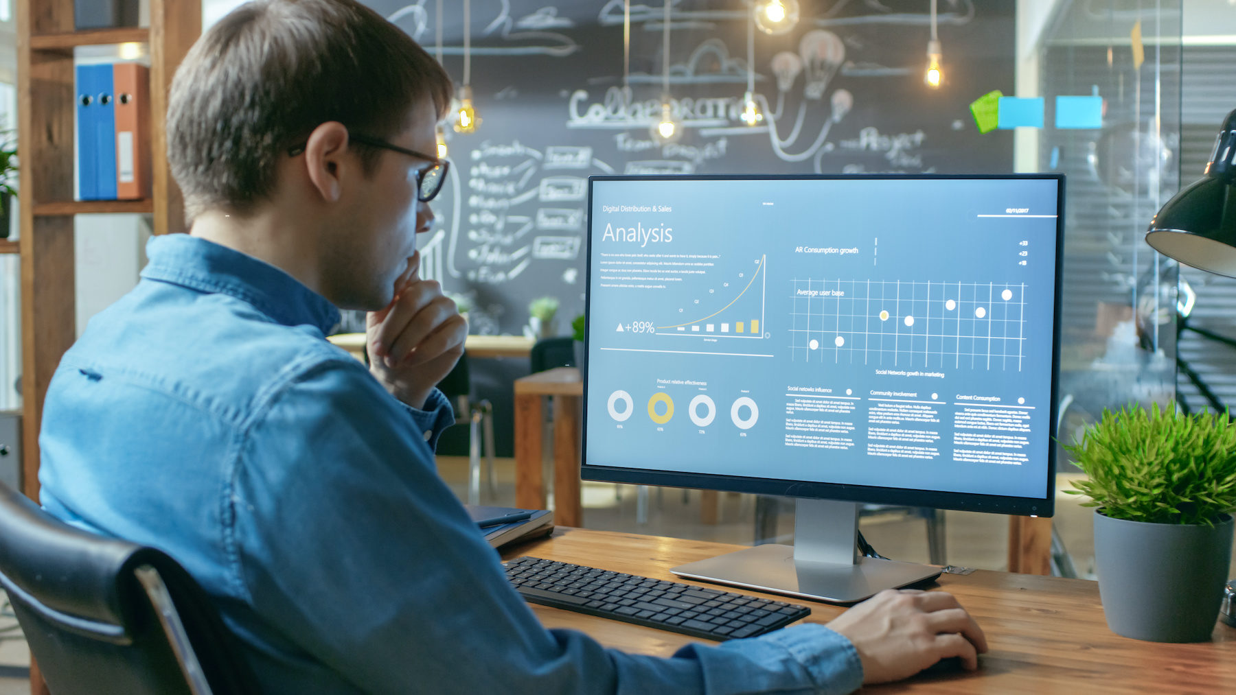 Financier Works on a Personal Computer Showing Statistics, Graphs and Charts. In the Background His Coworker and Creative Office.