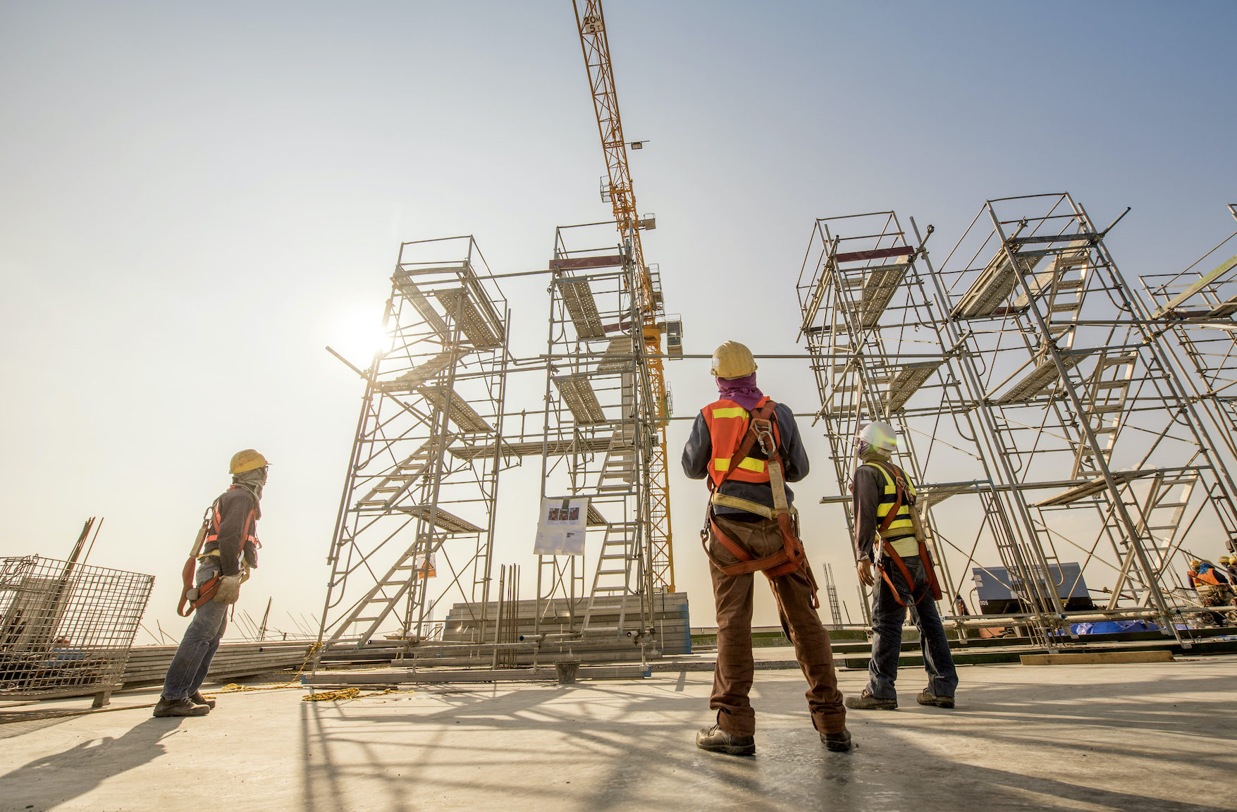 Construction engineers supervising progress of construction project stand on new concrete floor top roof and crane background