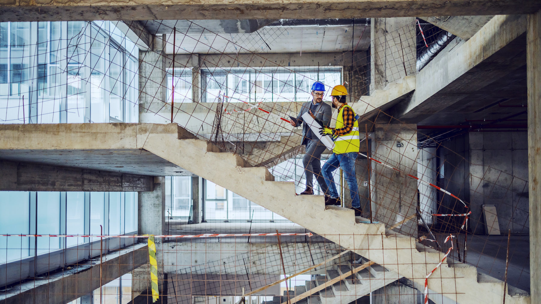 Construction worker and main architect climbing the stairs and talking about progress in construction of new building.